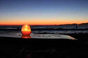 Ein Windlicht steht am Strand vor einem Sonnenuntergang